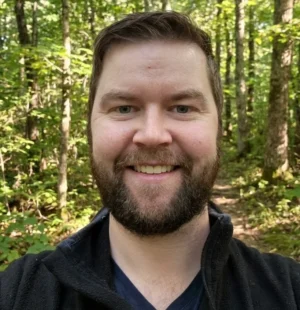 Profile shot of man with forest background. Man is smiling.